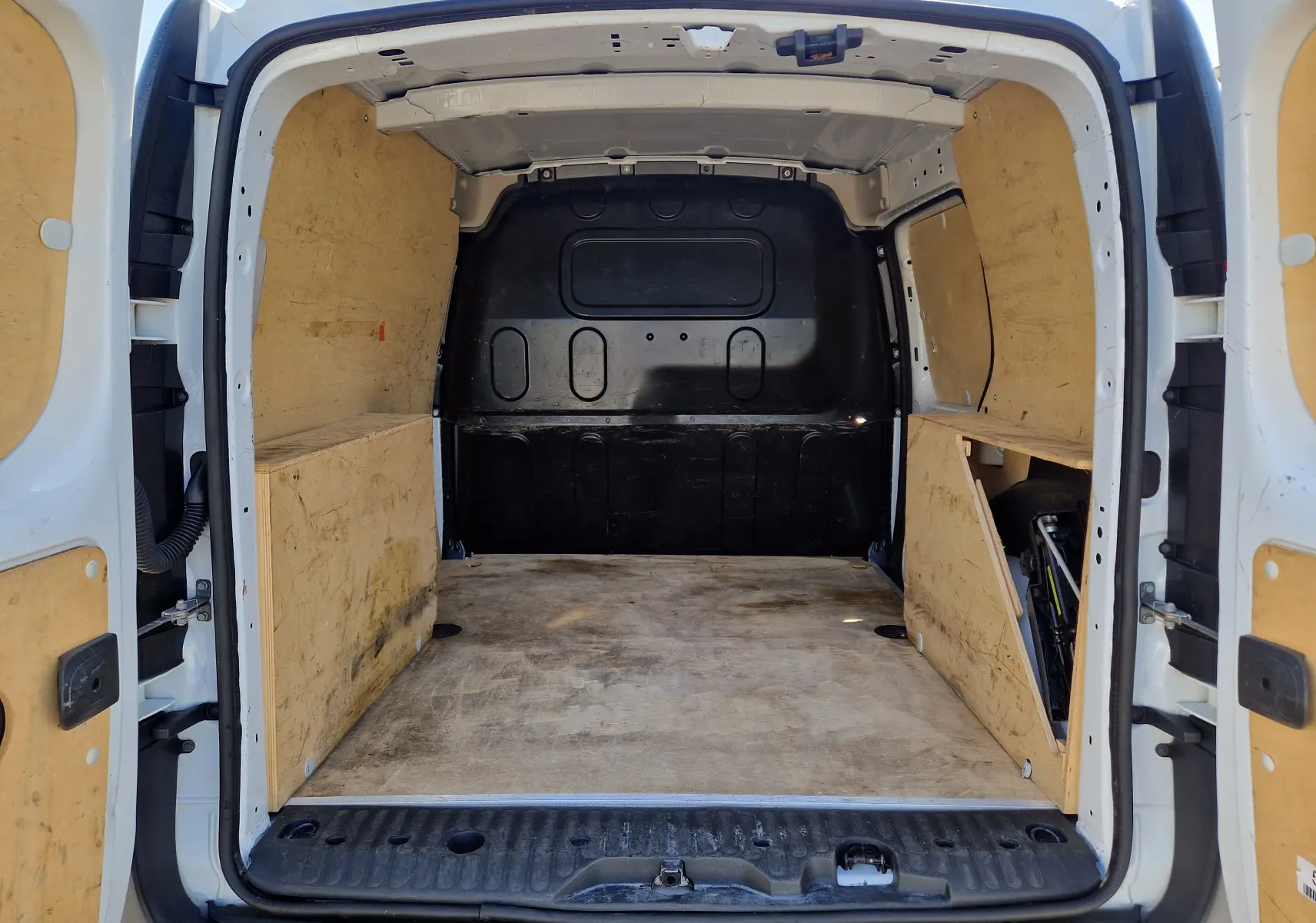 Vue arrière ouverte du Renault Kangoo blanc 2021, montrant l'espace de chargement avec aménagements en bois sur les côtés.