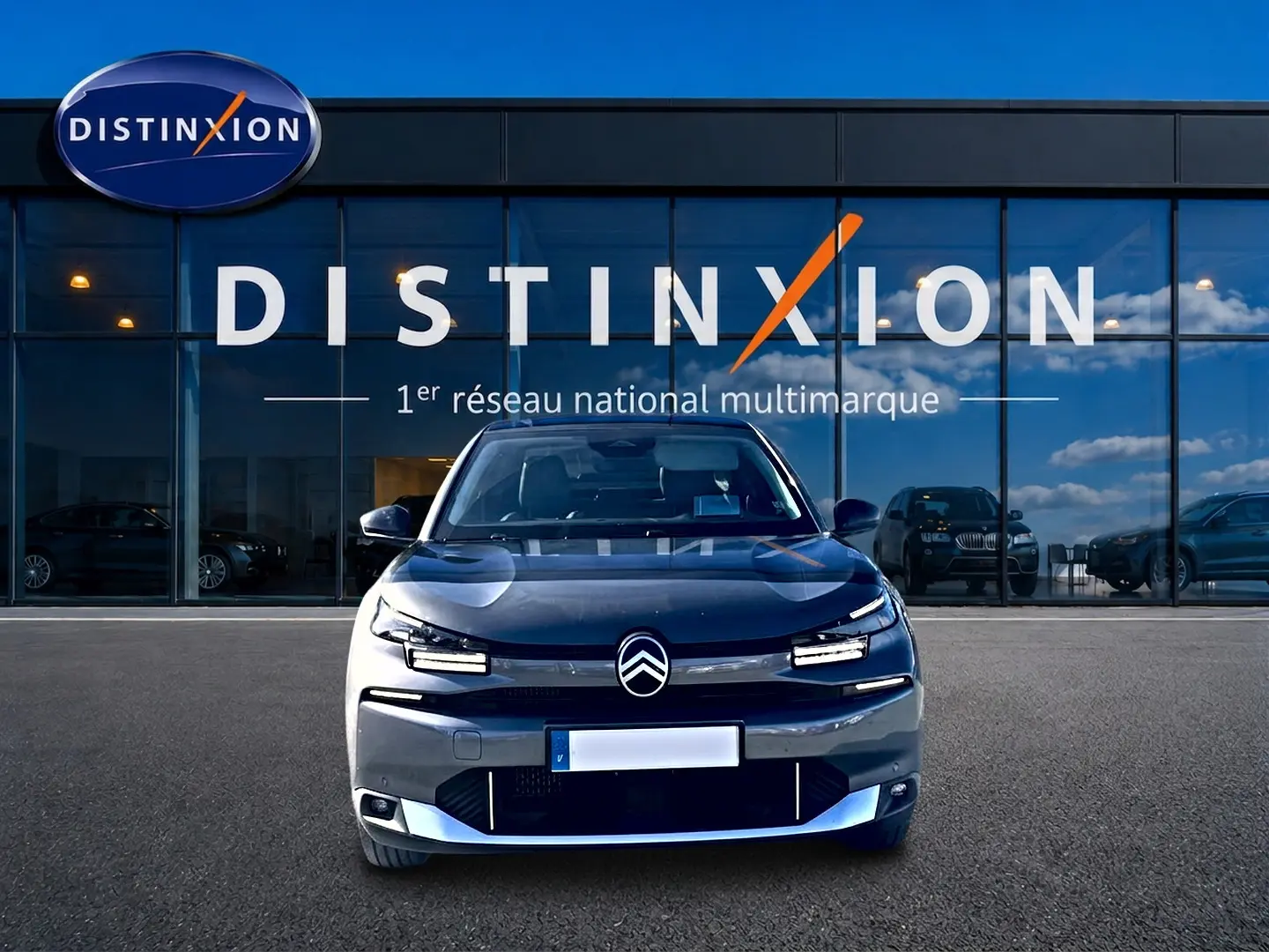 Vue frontale d'une Citroën C4 X gris mercure avec signature lumineuse LED, devant une vitrine Distinxion.