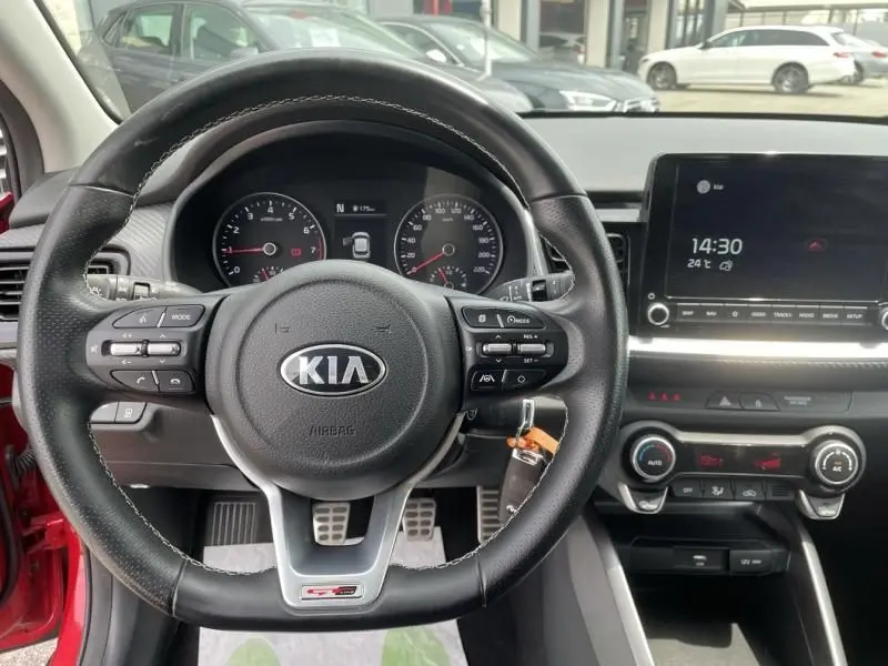 Volant KIA en gros plan avec tableau de bord et écran central, intérieur d'une voiture rouge visible au niveau de la portière.