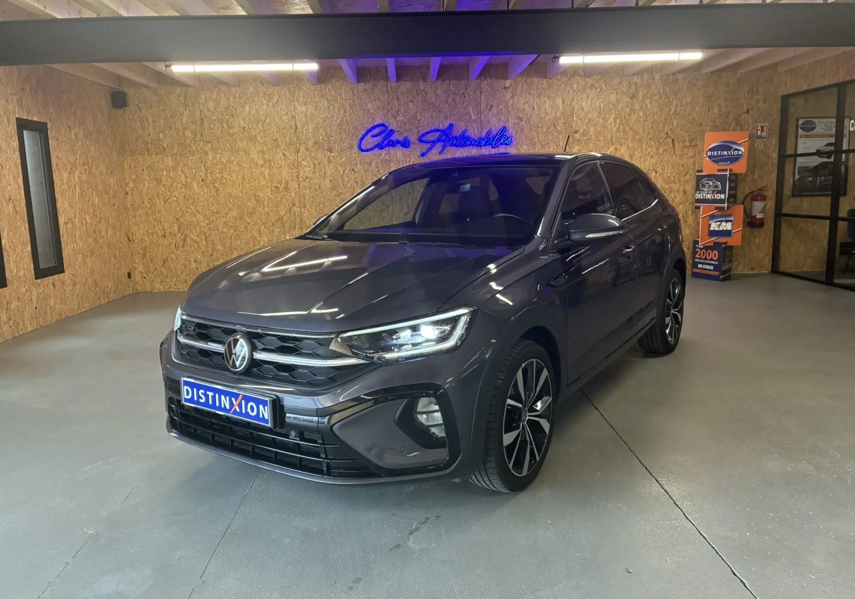 Volkswagen Taigo 1.5 TSI 150 R-LINE gris en 3/4 avant droit, avec jantes alliage et phares LED allumés.