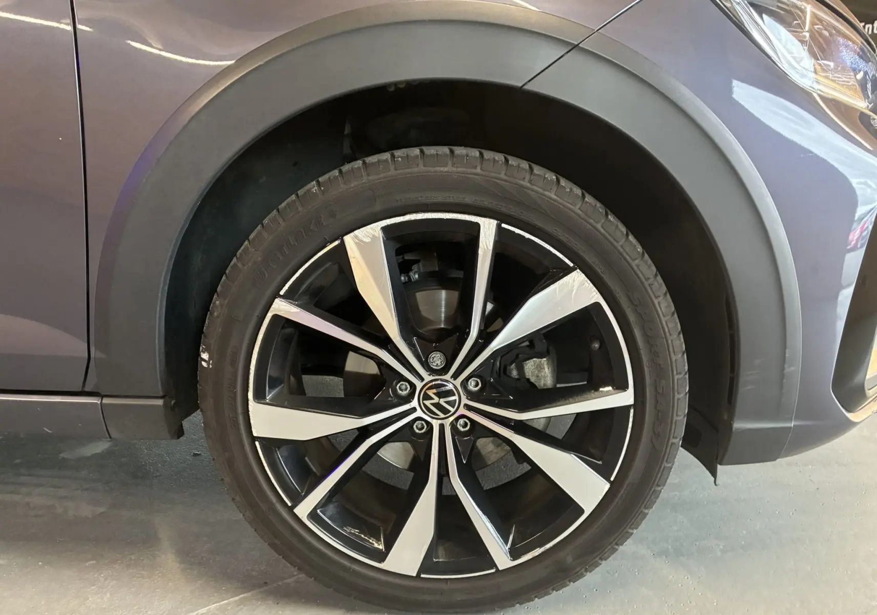 Gros plan sur la roue avant gauche du Volkswagen Taigo gris 2023, mettant en valeur la jante alliage noire et argentée R-LINE.