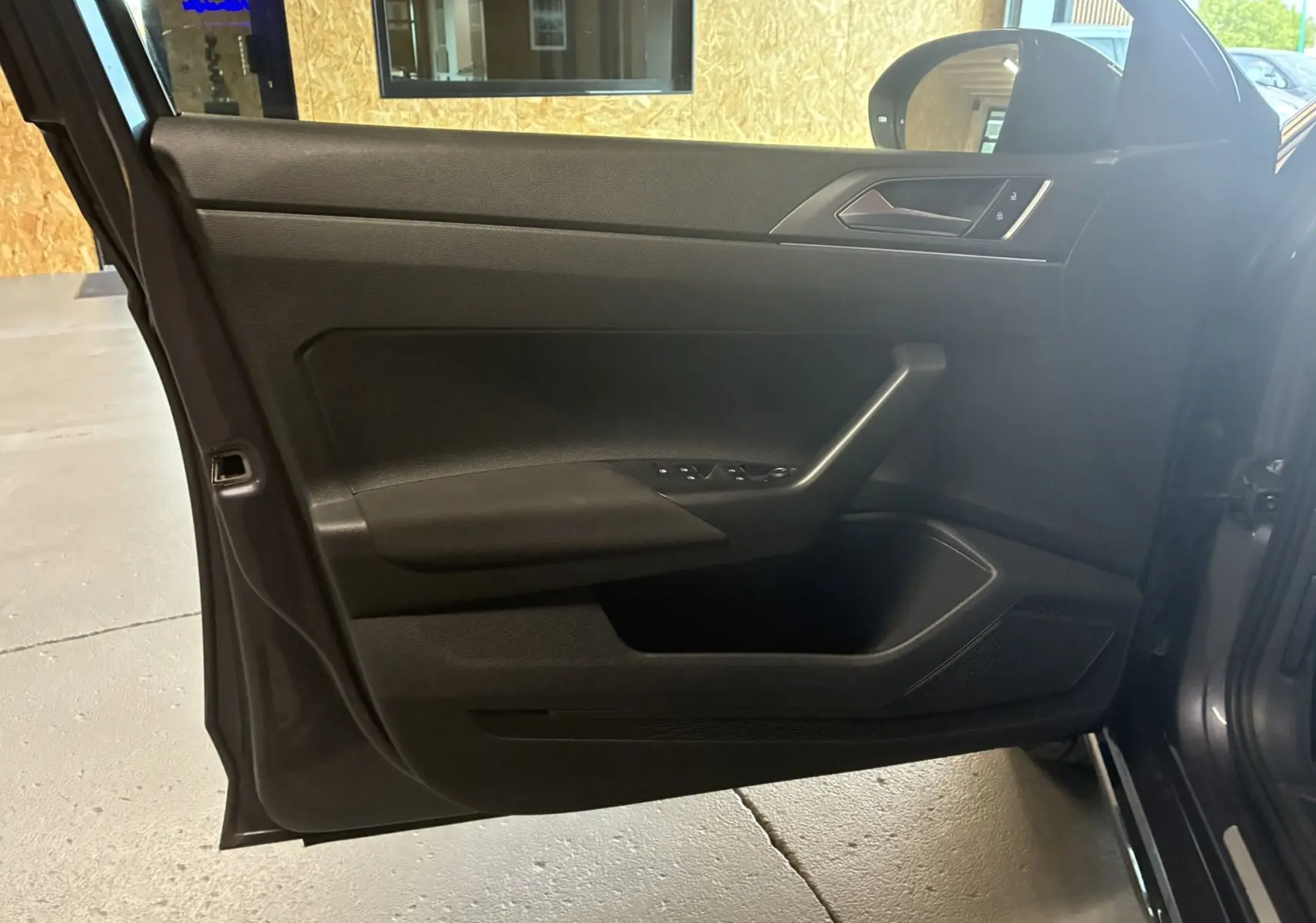 Porte avant gauche ouverte d'un Volkswagen Taigo gris 2023, montrant la garniture intérieure noire avec commandes électriques.