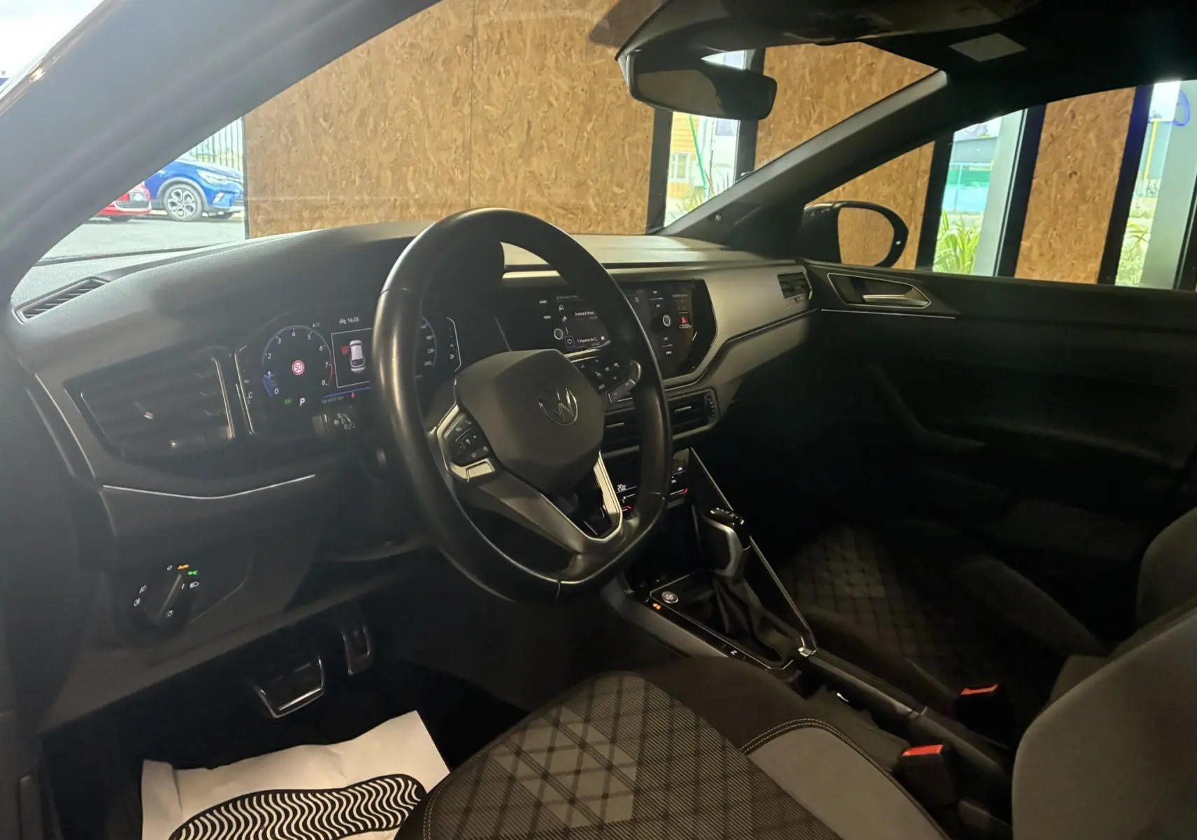 Intérieur avant droit du Volkswagen Taigo gris 2023, volant multifonction, tableau de bord digital et sièges tissu gris-noir.