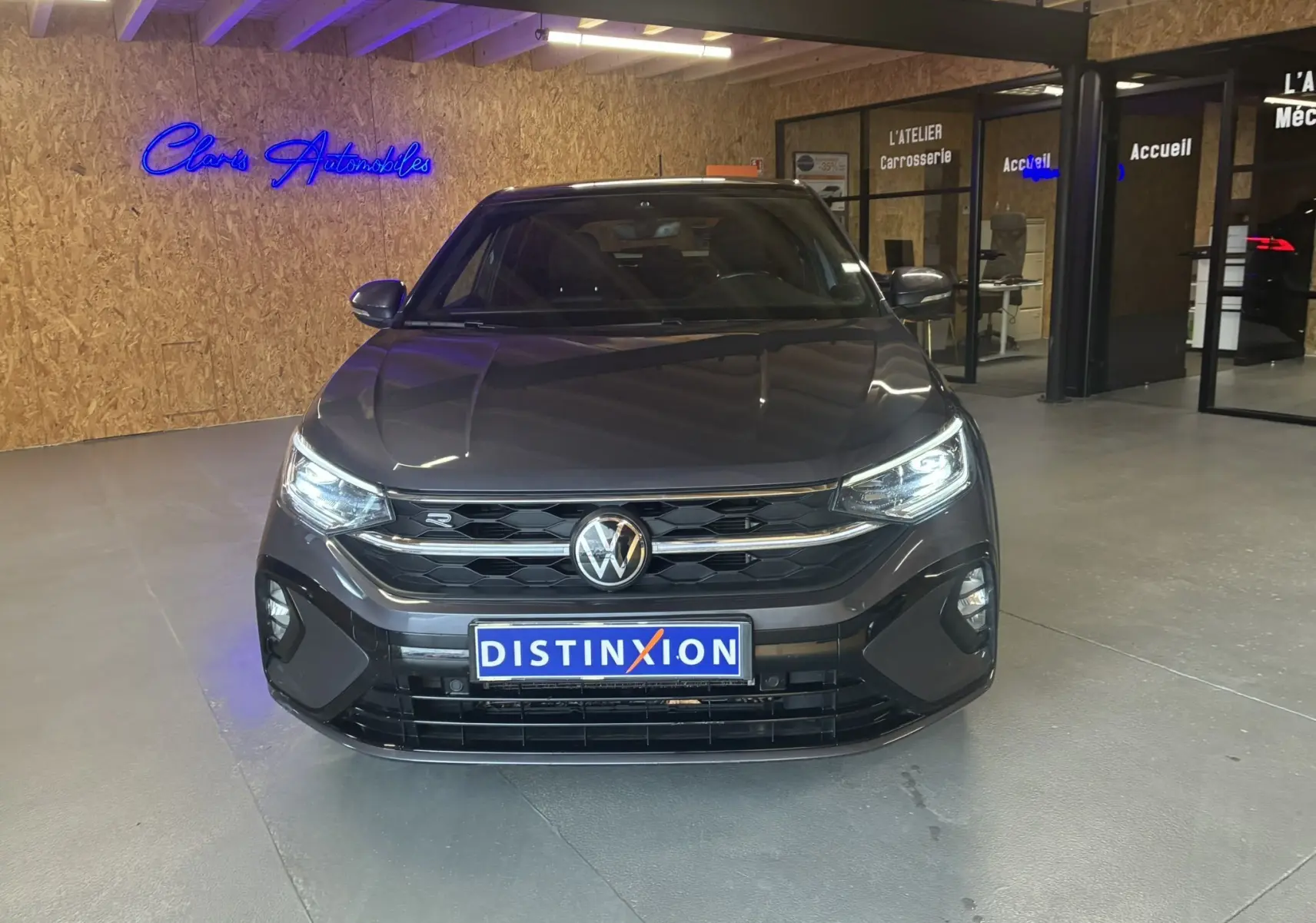 Vue de face d'un Volkswagen Taigo gris 2023 en version R-Line, avec calandre noire et phares allumés dans un showroom.