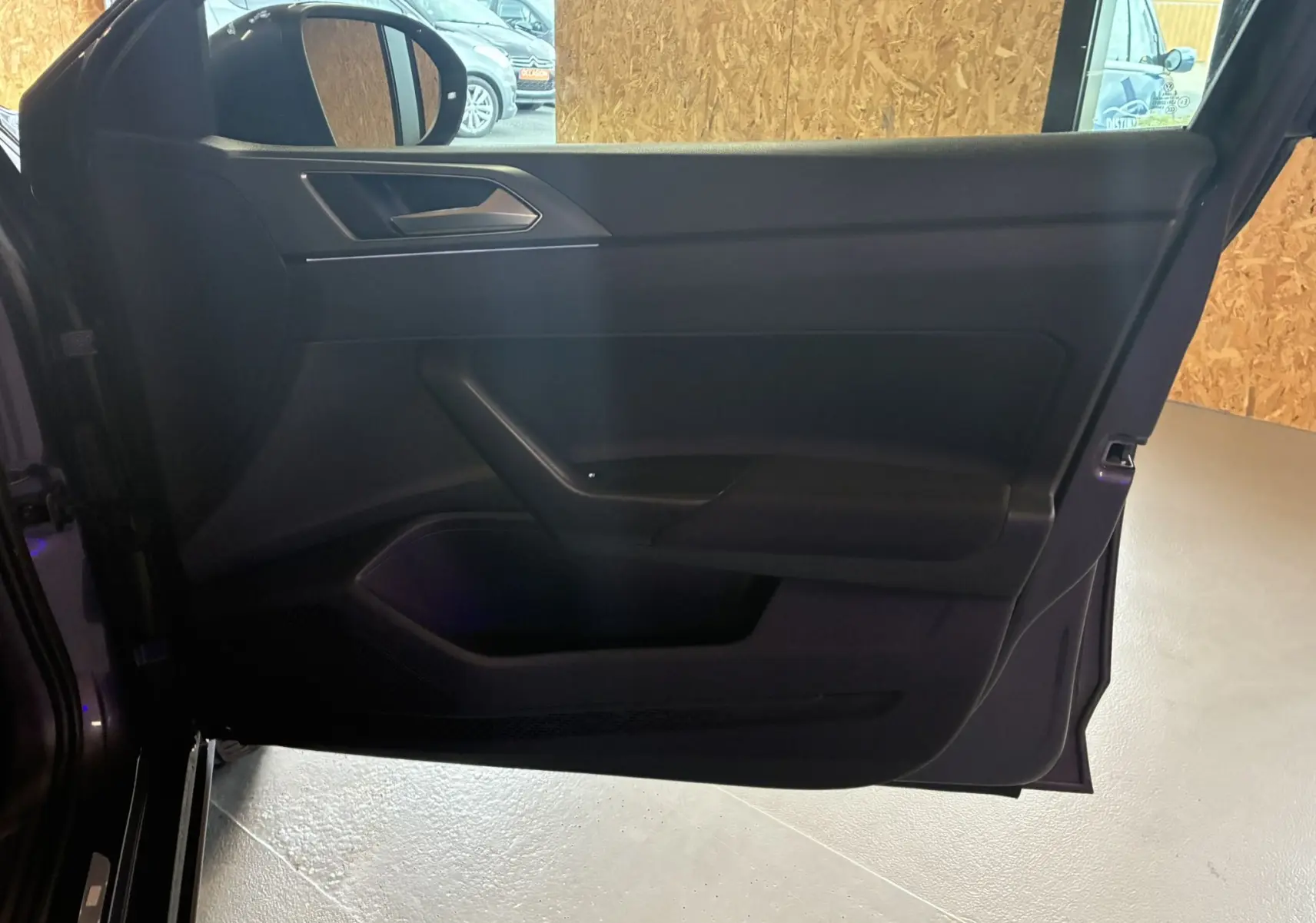 Vue intérieure de la porte côté gauche d'un Volkswagen Taigo gris 2023, avec garniture noire et poignée intégrée.