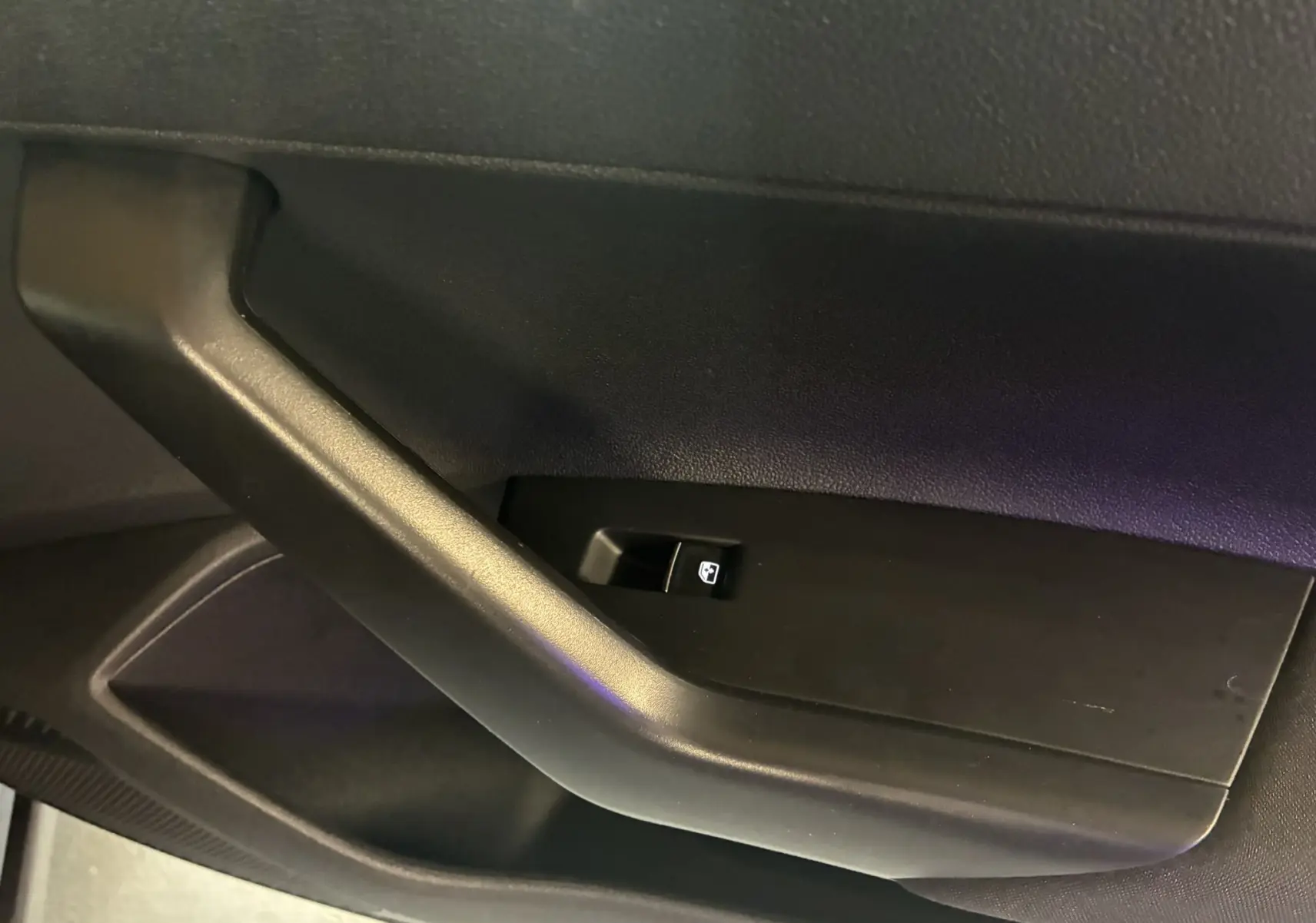 Gros plan sur la poignée intérieure noire et le bouton de commande de vitre du côté conducteur du Volkswagen Taigo gris 2023.