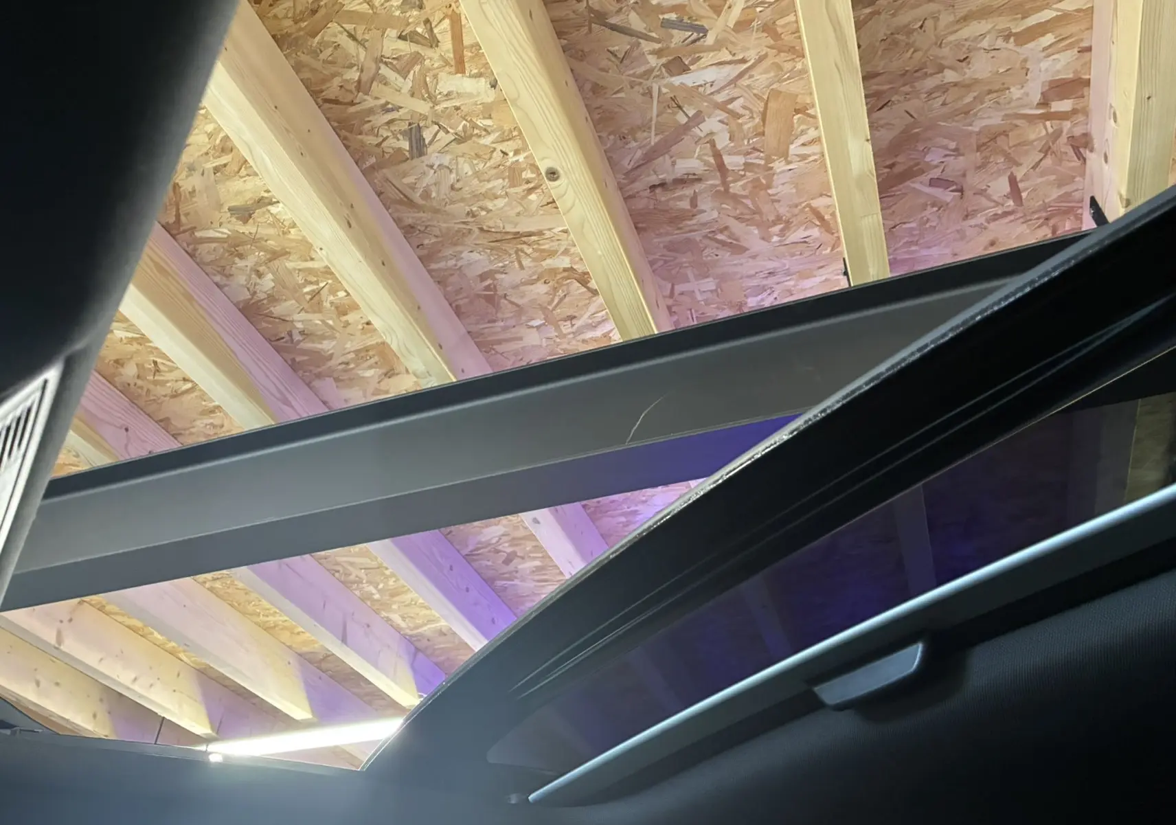 Toit panoramique ouvert vu de l'intérieur du Volkswagen Taigo gris, sous une charpente en bois.