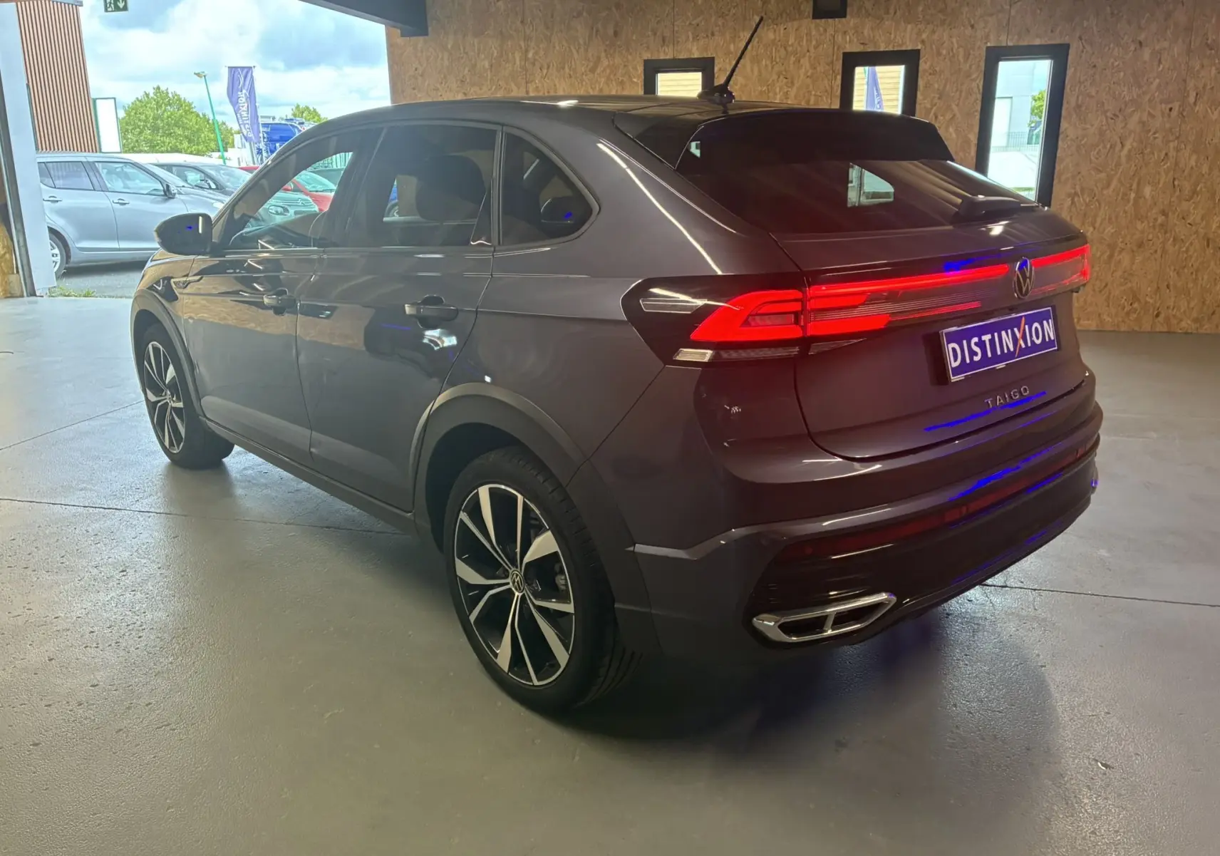 Volkswagen Taigo gris en 3/4 arrière droit dans un garage, avec feux arrière LED allumés et jantes noires distinctives.