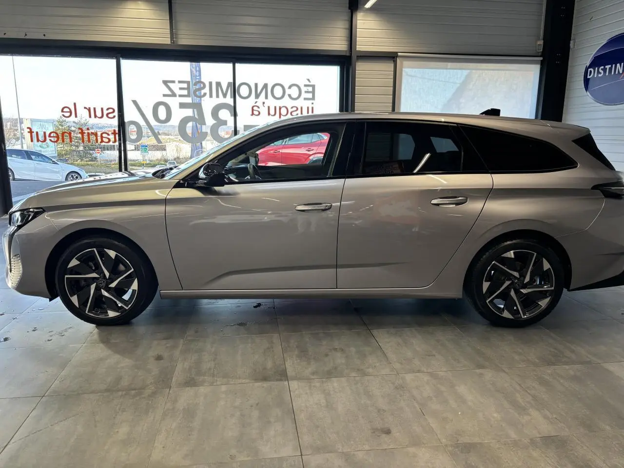 Profil droit d'une Peugeot 308 SW gris clair métallisé, avec jantes alliage noires et toit noir en showroom.