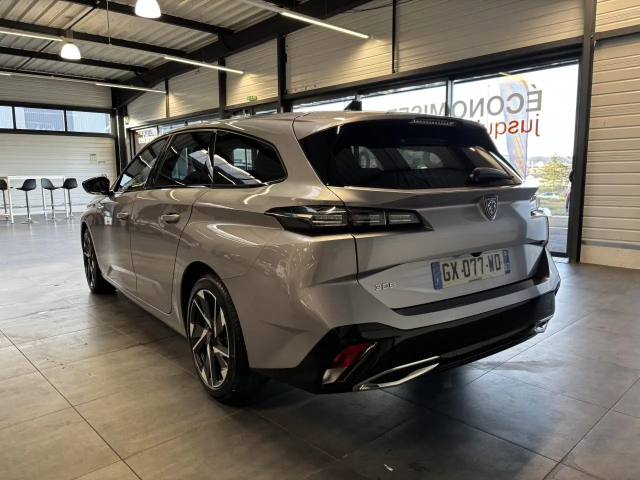 Vue 3/4 arrière droite d'une Peugeot 308 SW gris clair métallisé Artense en intérieur avec jantes alliage 17 pouces.