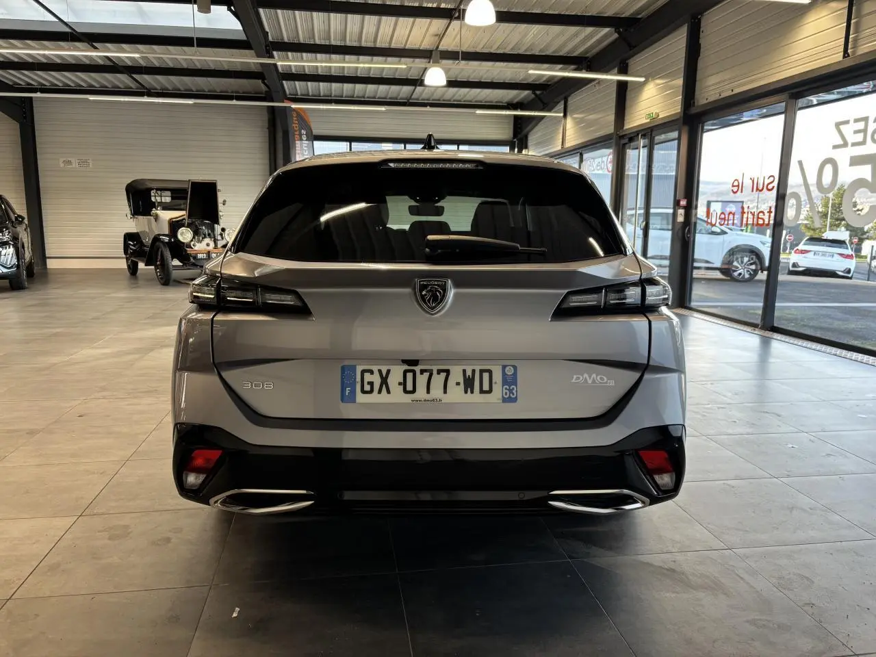 Vue arrière d'une Peugeot 308 SW gris clair métallisé exposée en showroom, avec feux arrière LED et double sortie d'échappement.