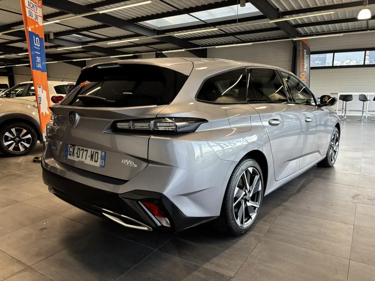 Vue 3/4 arrière droite d’un Peugeot 308 SW gris clair métallisé avec jantes alliage et feux LED distinctifs en intérieur showroom.