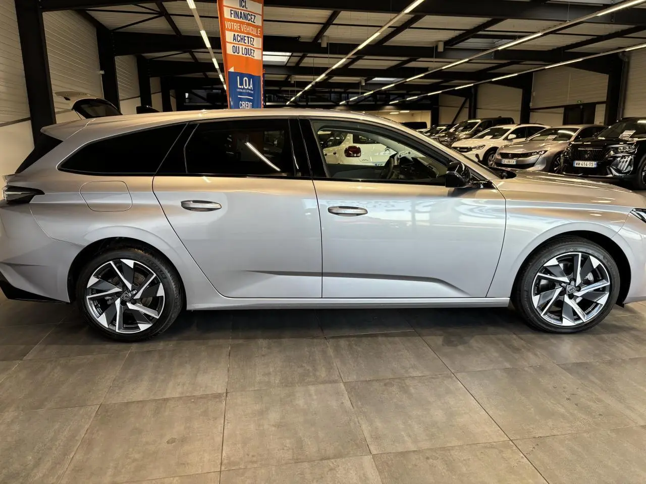 Peugeot 308 SW gris clair métal Artense vue de profil côté gauche en intérieur avec jantes alliage 17 pouces.