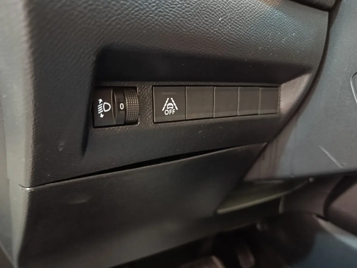 Détail des commandes d’éclairage et d’aide à la conduite sur tableau de bord noir du Peugeot 208 électrique.