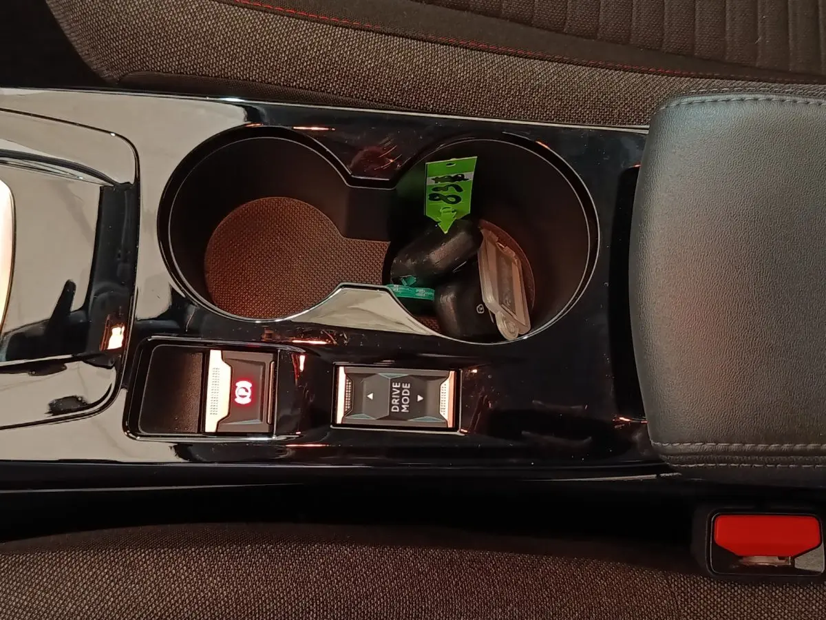 Gros plan sur la console centrale noire brillante de la Peugeot 208 électrique avec boutons frein à main et mode de conduite.