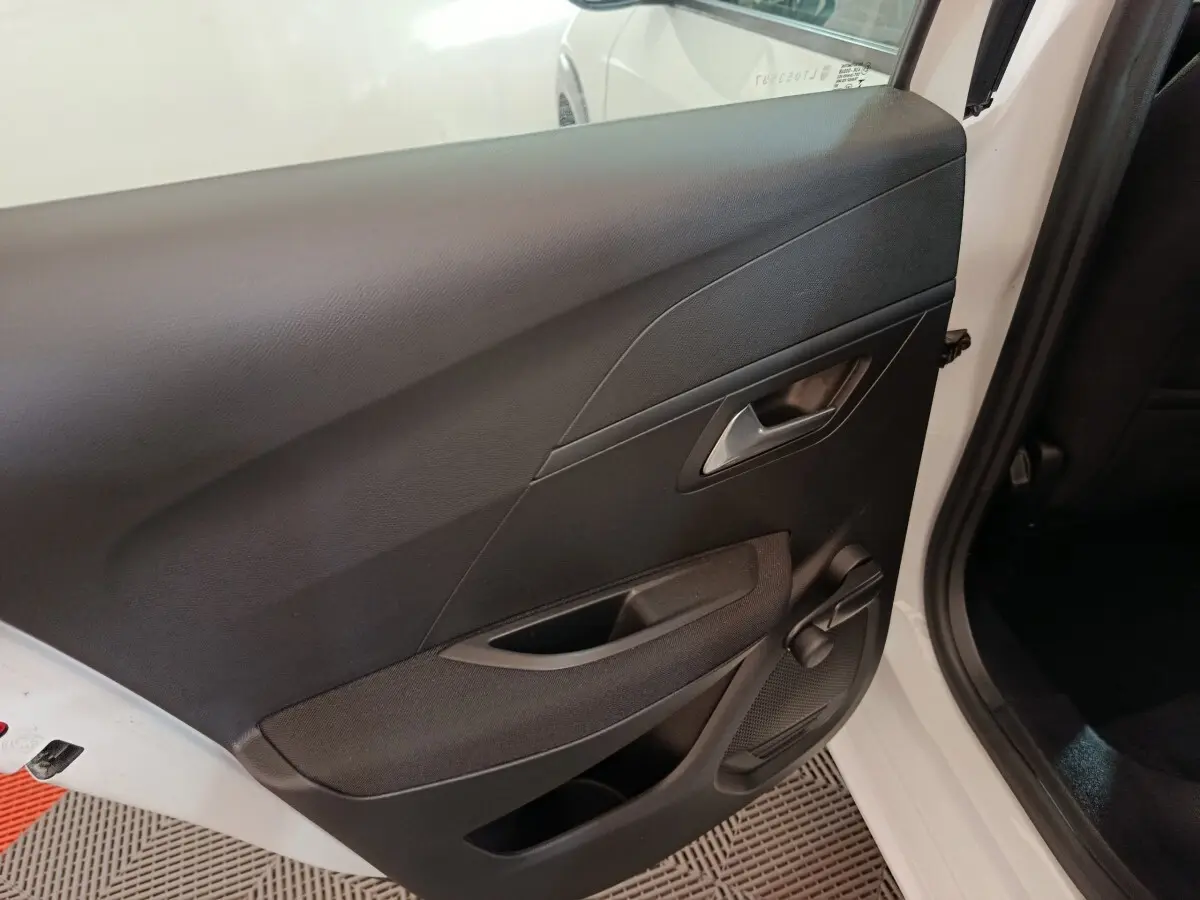 Vue intérieure sur la porte arrière droite noire d'une Peugeot 208 électrique blanche, avec poignée et manivelle de vitre.