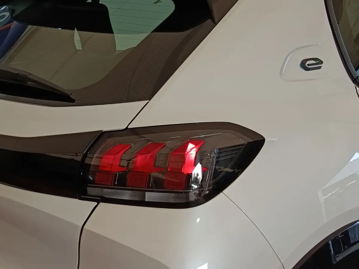 Gros plan sur le feu arrière droit rouge d’une Peugeot 208 électrique blanche, avec logo « e » sur l’aile arrière.