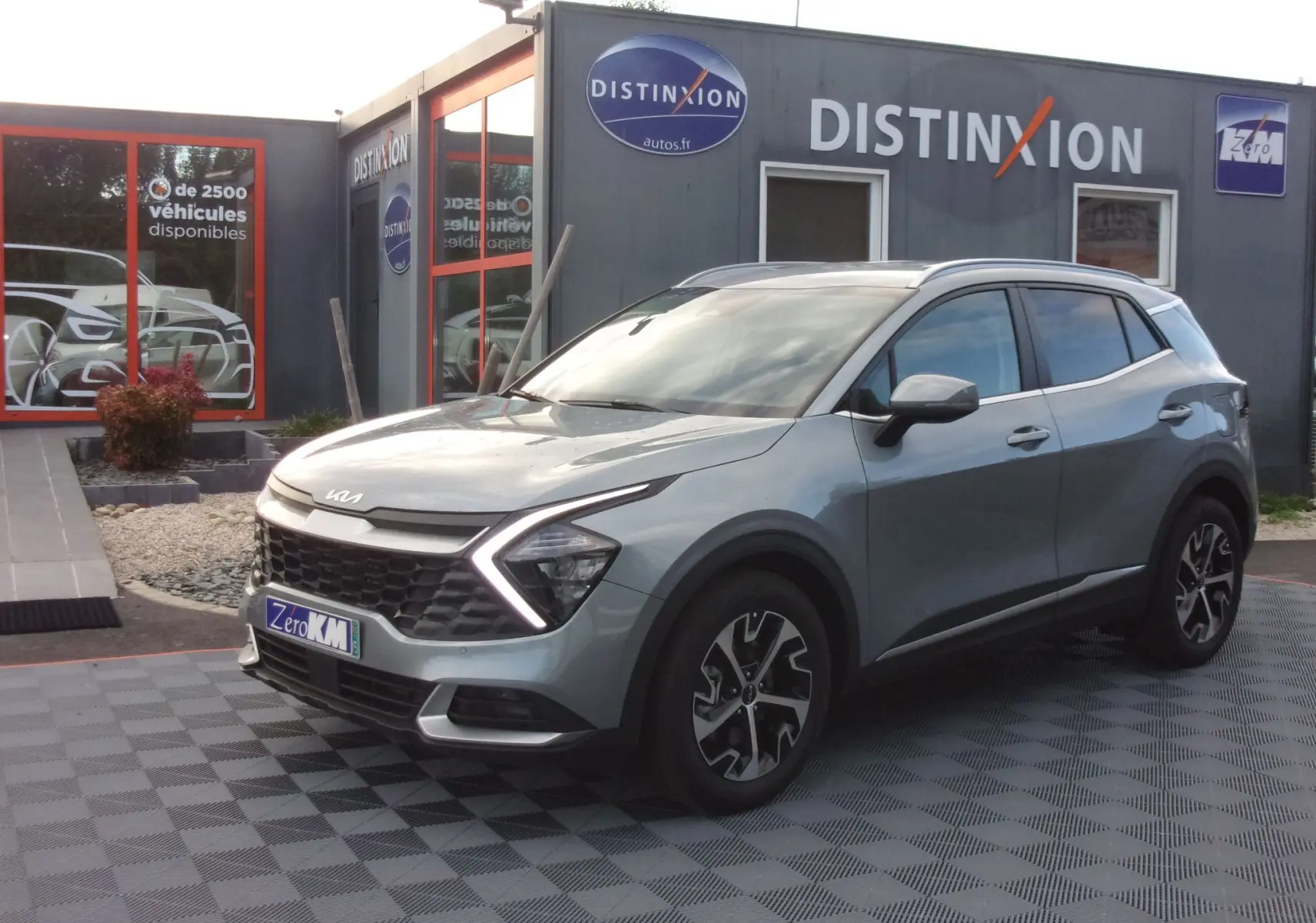 KIA Sportage gris perle en 3/4 avant droit, avec calandre distinctive et feux LED en forme de flèche.