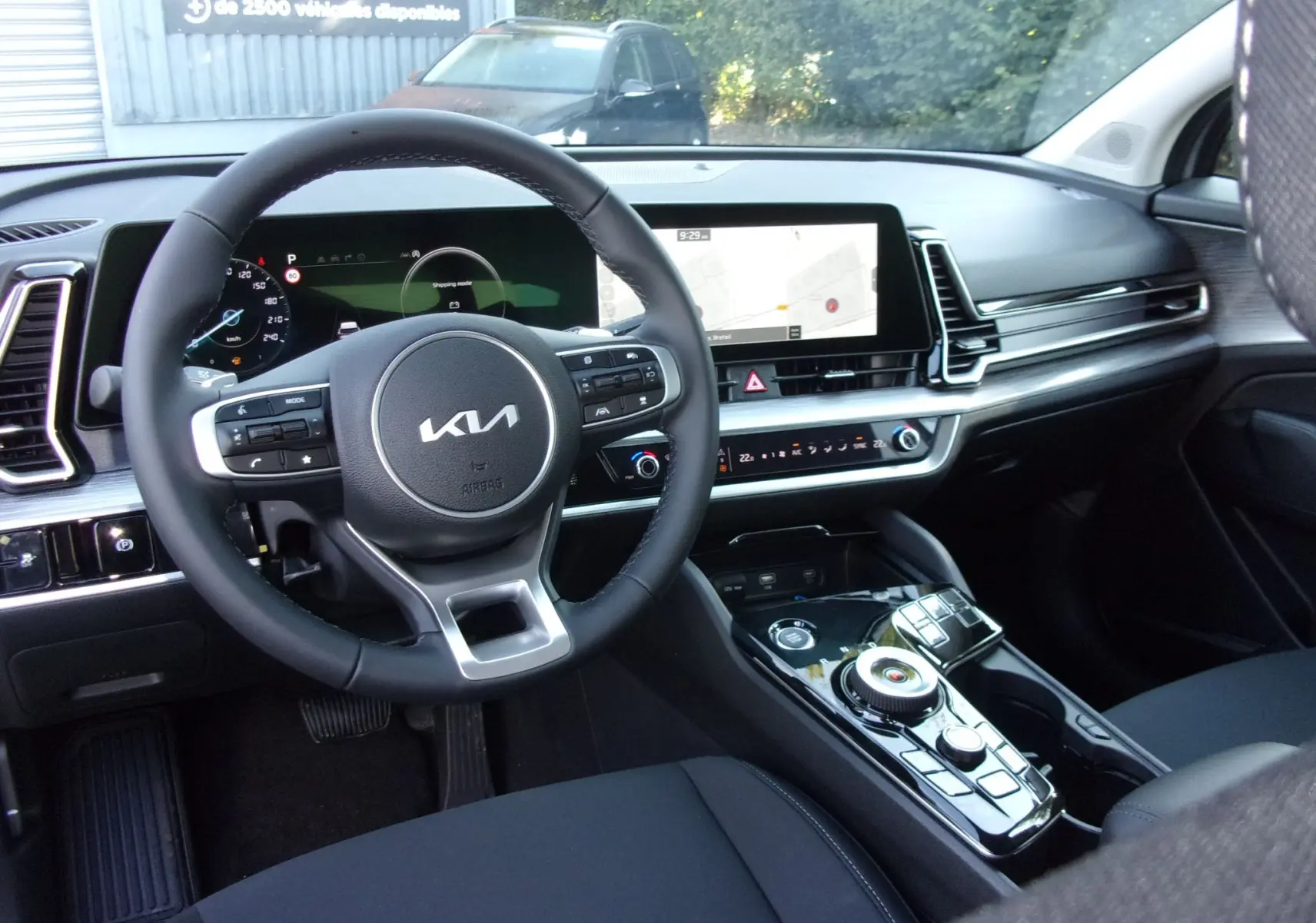 Intérieur du Kia Sportage 2025 gris perle, vue du poste de conduite avec volant multifonction et écran tactile GPS.