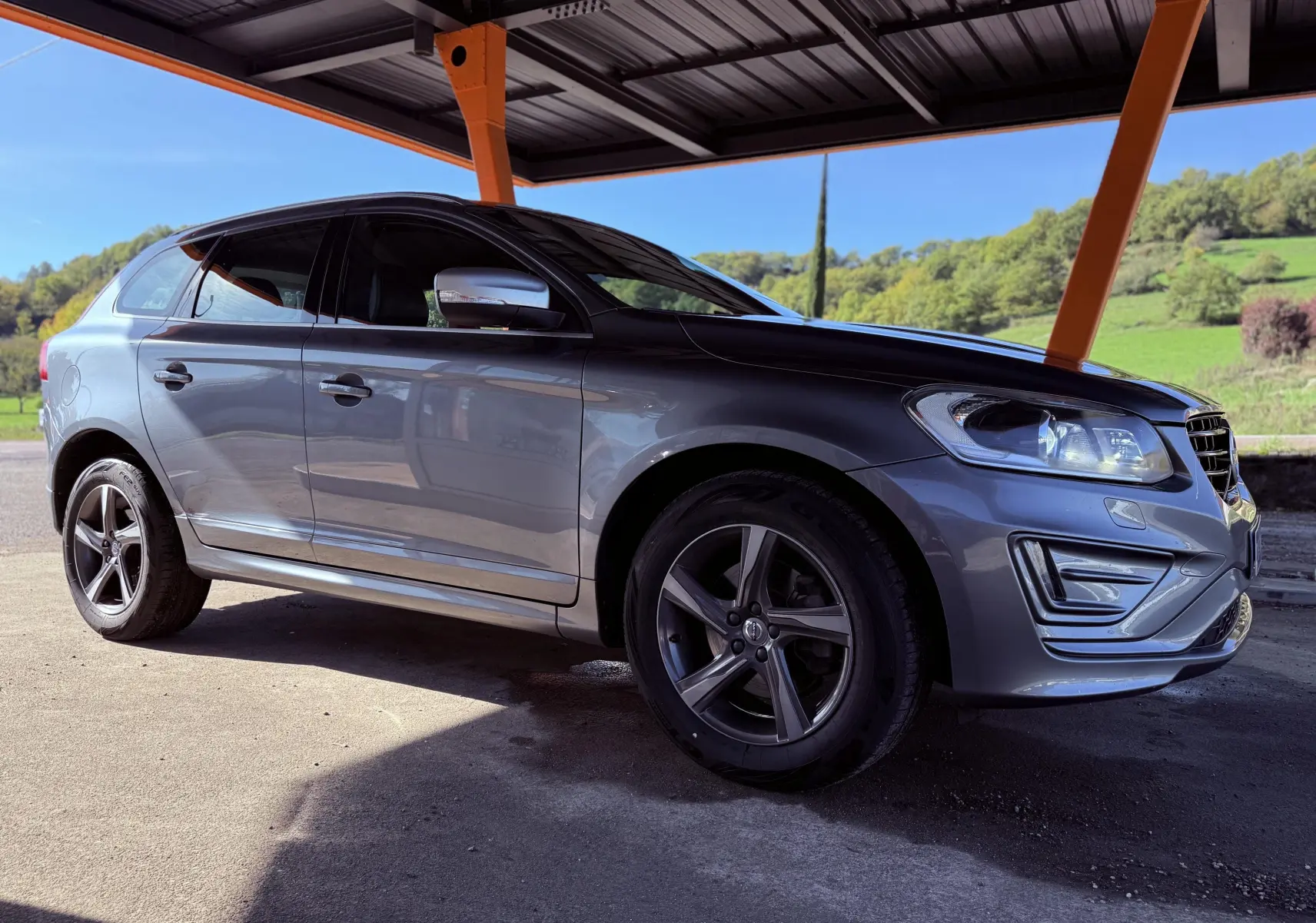 Vue 3/4 avant droit d'un Volvo XC60 gris métallisé 2016 sous abri, mettant en valeur ses jantes alliage et phares LED.