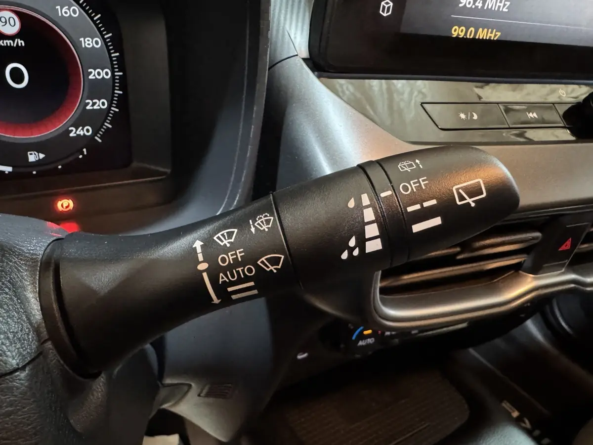 Gros plan sur la commande des essuie-glaces du Nissan Juke gris clair 2025, avec tableau de bord et écran tactile en arrière-plan.