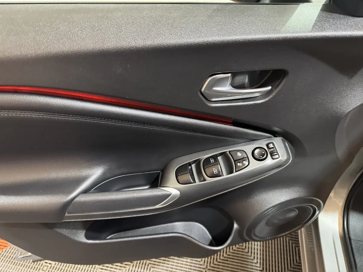 Vue intérieure côté gauche de la porte avant gris clair du Nissan Juke avec commandes vitres et bandeau lumineux rouge.