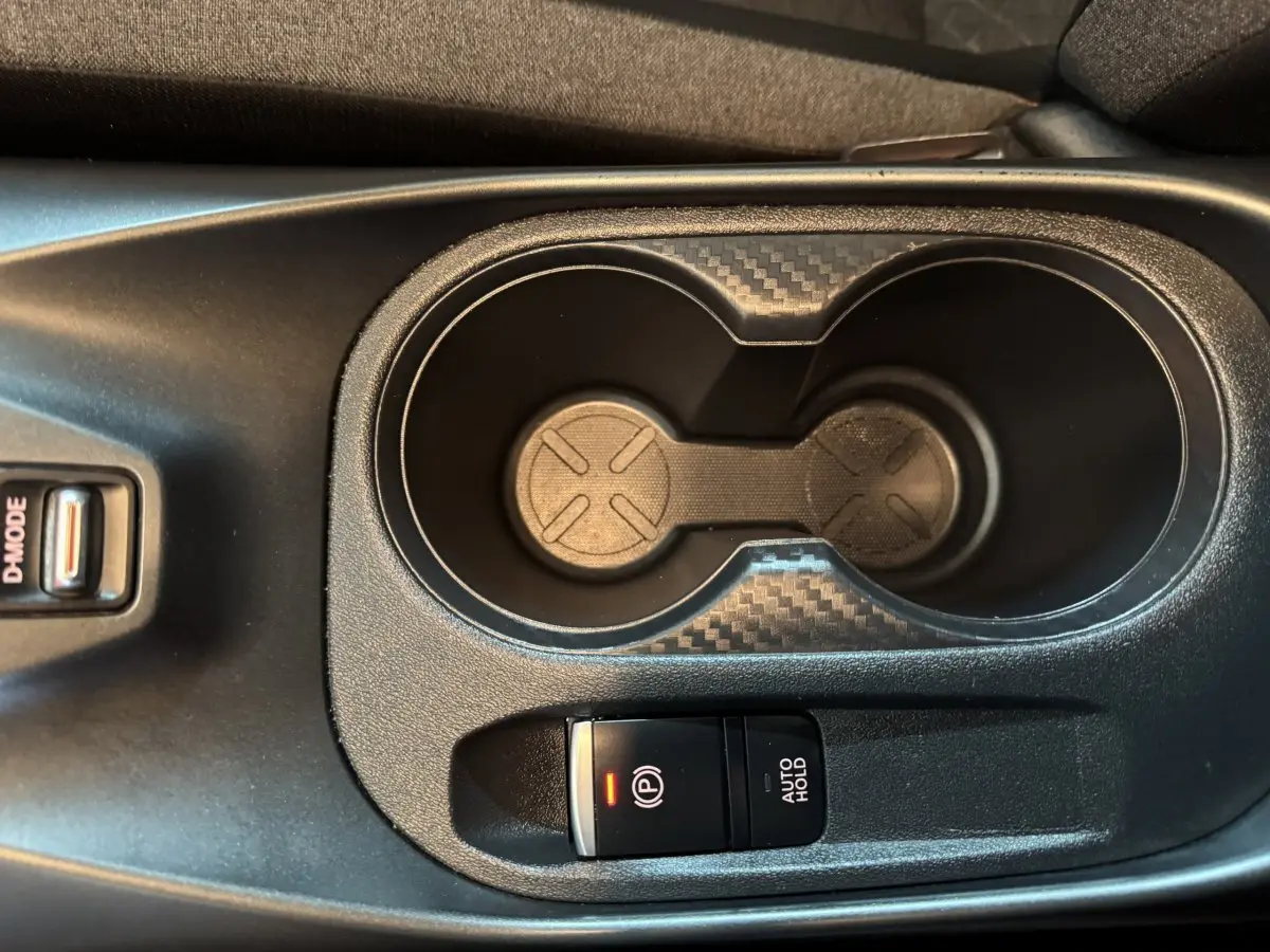 Gros plan sur la console centrale du Nissan Juke gris clair 2025, avec porte-gobelets et frein à main électrique.