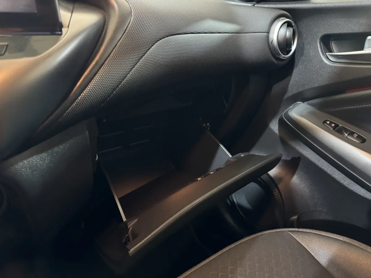 Vue intérieure côté passager du Nissan Juke 2025 gris clair, avec boîte à gants ouverte et détails de la porte.