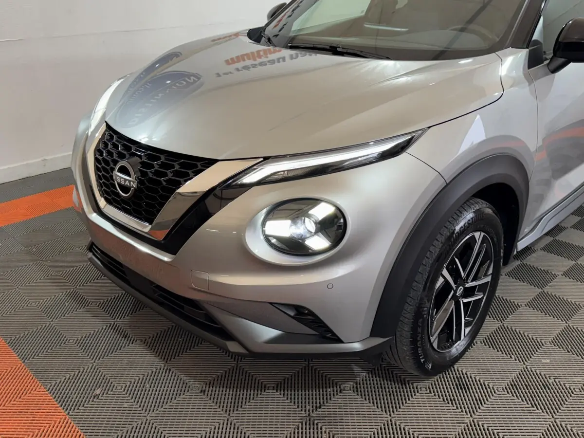 Vue 3/4 avant droit du Nissan Juke gris clair avec phares LED allumés et calandre en V chromée.