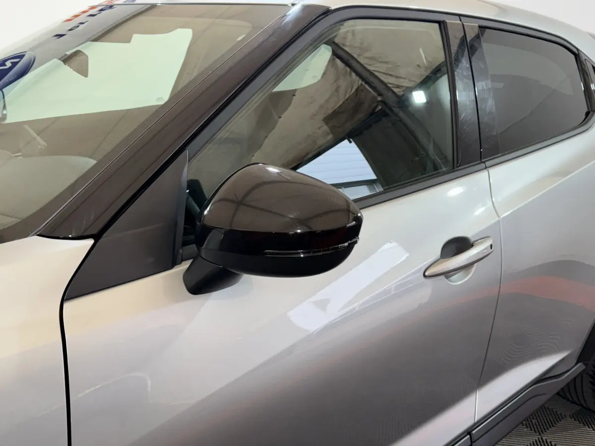 Vue rapprochée du côté gauche d’un Nissan Juke gris clair avec rétroviseur noir brillant et poignée de porte visible.