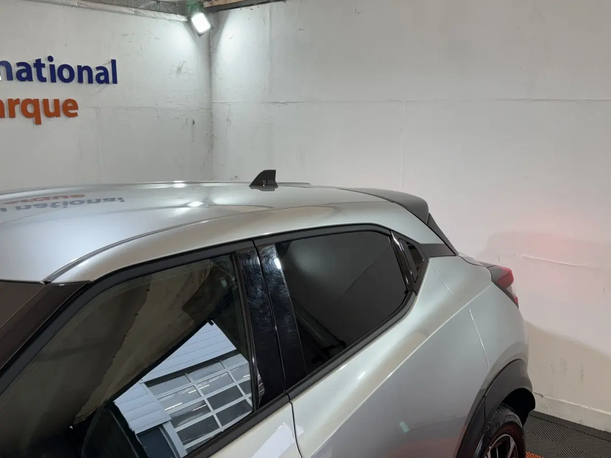 Vue latérale arrière droite du Nissan Juke gris clair avec vitres teintées et toit compact en intérieur showroom.