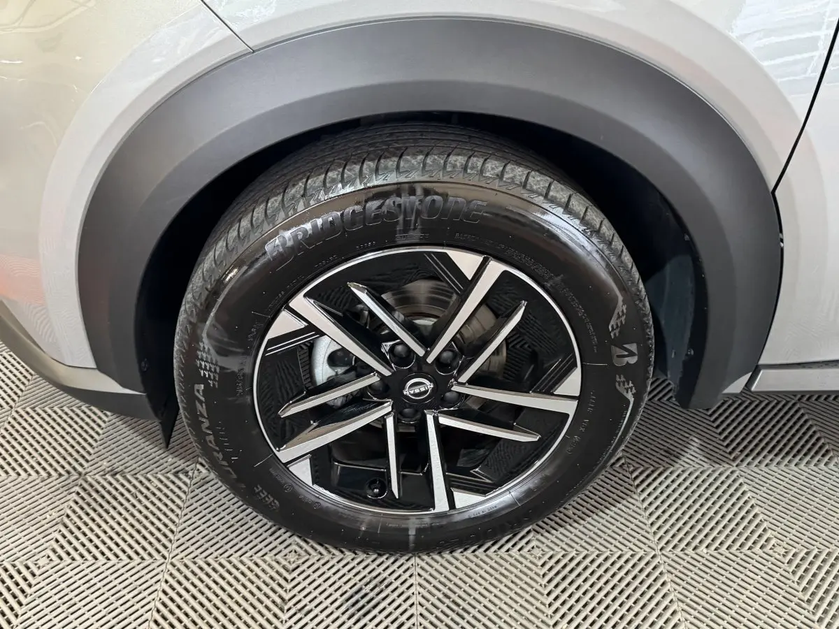 Gros plan sur la roue avant droite du Nissan Juke gris clair, mettant en valeur la jante alliage noire et argentée.