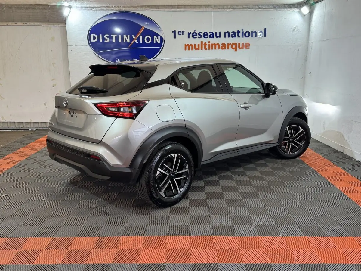 Vue 3/4 arrière droite d'un Nissan Juke gris clair 2025 avec jantes noires et vitres teintées en intérieur showroom.