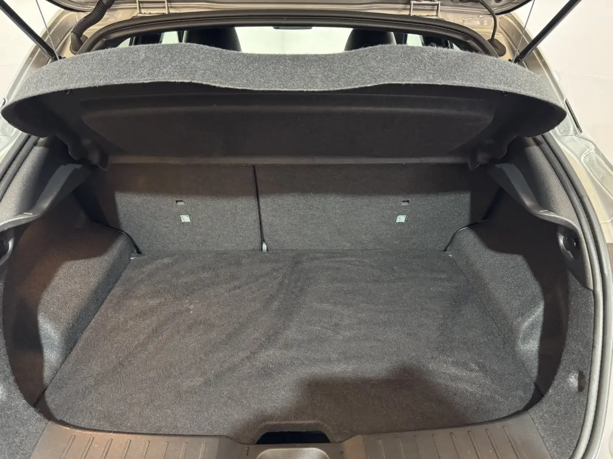 Coffre ouvert du Nissan Juke gris clair 2025, vue de l'arrière montrant l'espace de chargement vide et la tablette arrière.