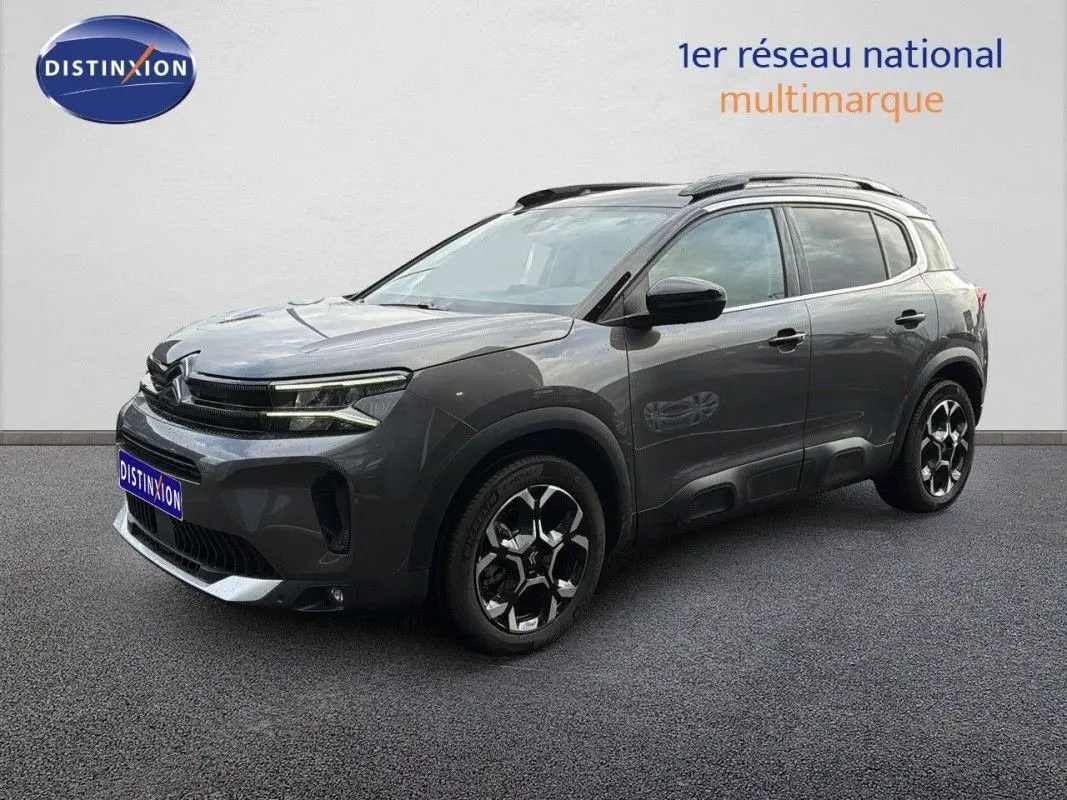 Citroën C5 Aircross Hybrid gris platinium en 3/4 avant droit avec jantes bicolores et barres de toit noires.