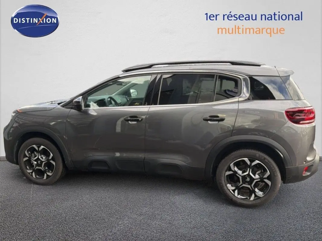 Vue de profil côté gauche du Citroën C5 Aircross Hybrid gris platinium avec jantes bi-ton et barres de toit.