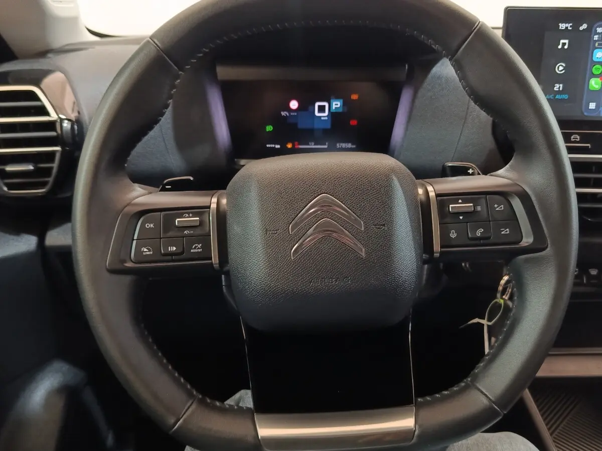 Vue rapprochée du volant cuir noir de la Citroën C4 X 2023 avec commandes multifonctions et tableau de bord digital.