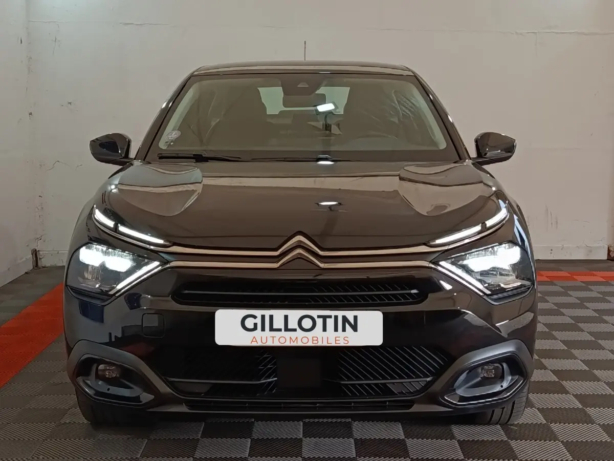 Vue frontale d'une Citroën C4 X noire 2023 avec phares LED allumés et calandre distinctive en intérieur showroom.