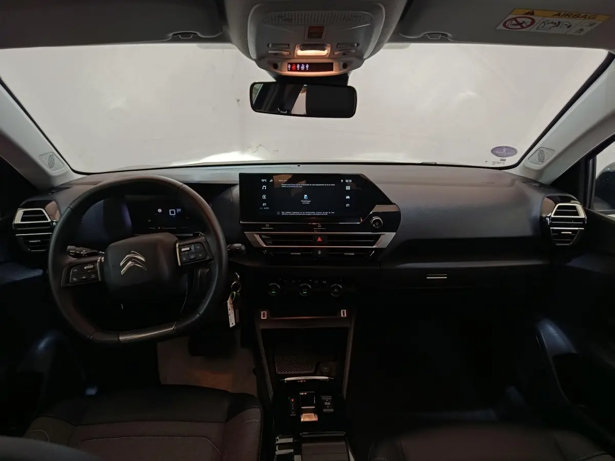 Vue intérieure avant du tableau de bord noir du Citroën C4 X 2023 avec écran tactile central et volant cuir multifonctions.