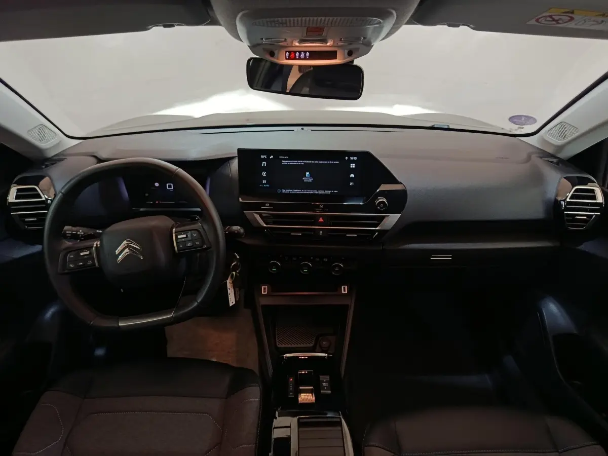 Vue intérieure frontale du tableau de bord noir du Citroën C4 X 2023 avec écran tactile central et volant multifonctions cuir.