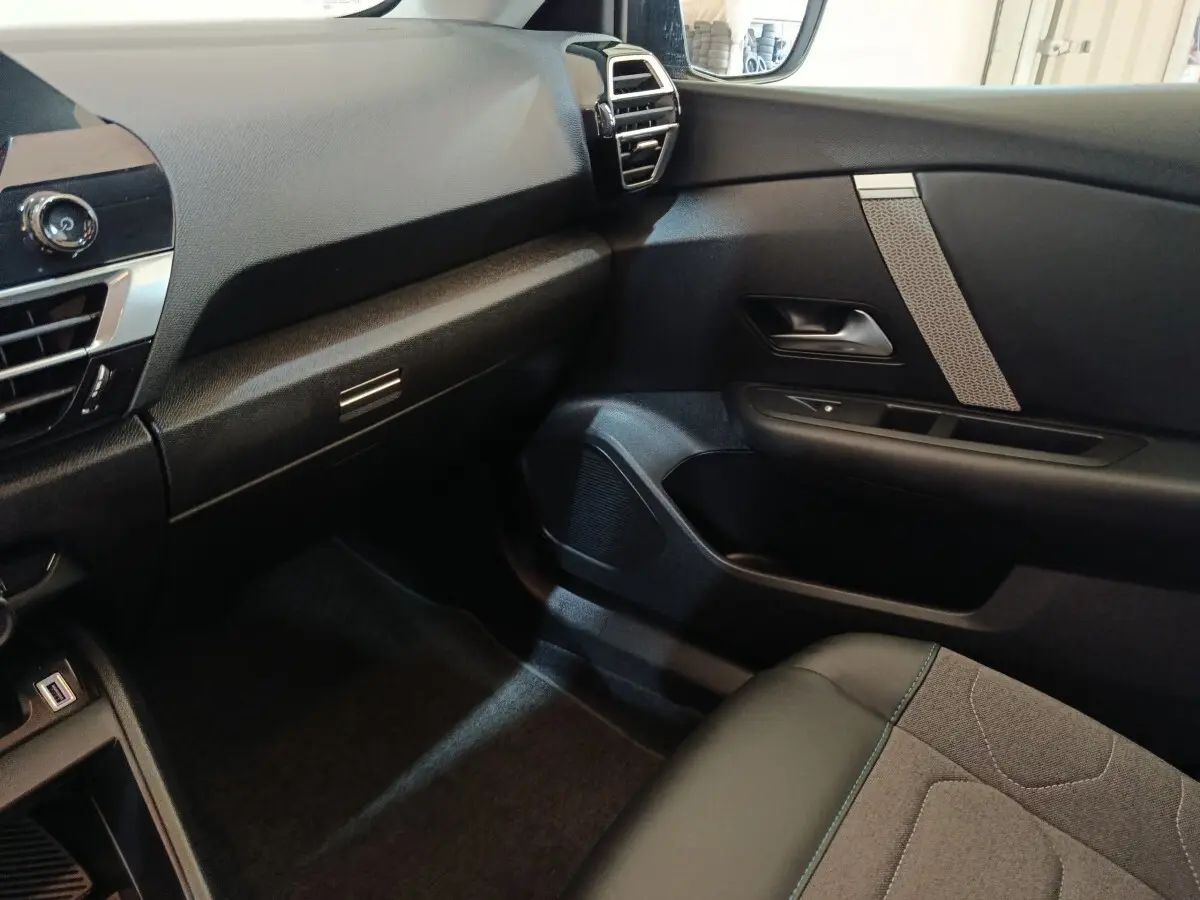 Intérieur côté passager du Citroën C4 X 2023, montrant tableau de bord et porte avec détails tissu et plastique noir.