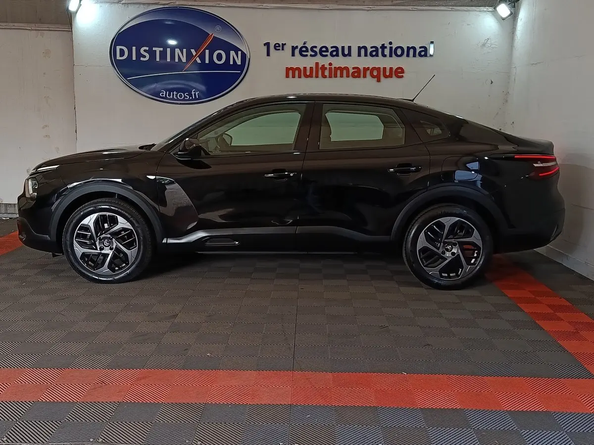 Vue latérale gauche d'une Citroën C4 X noire 2023 dans un showroom, soulignant ses lignes fluides et ses jantes modernes.