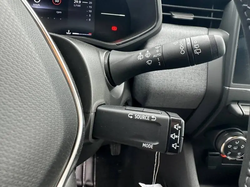 Gros plan sur les commandes au volant côté gauche du tableau de bord d’une Renault Clio gris 2025, boîte manuelle.