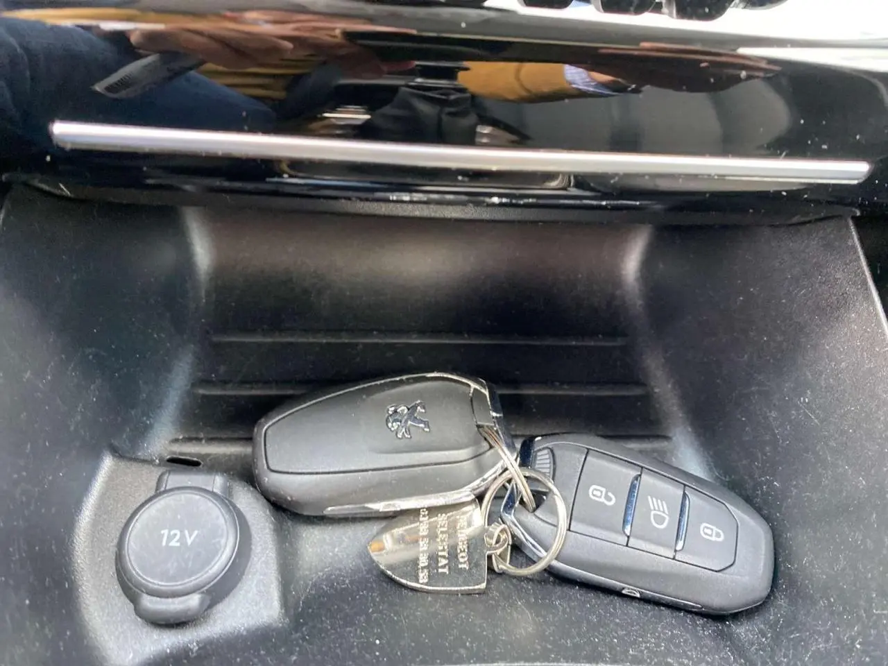 Gros plan sur les deux télécommandes noires Peugeot posées près de la prise 12V dans la console avant du véhicule.