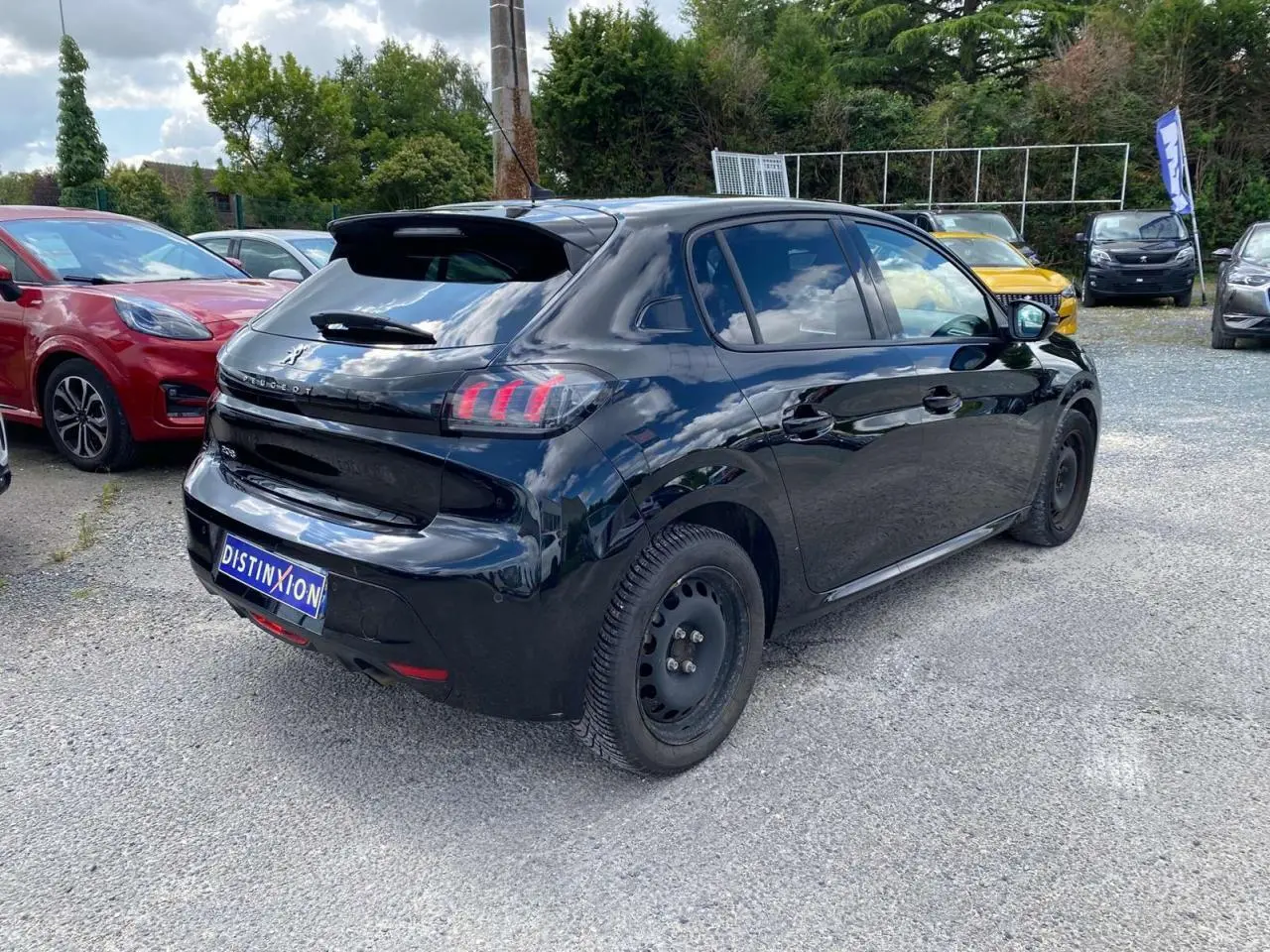 Peugeot 208 noire vue en 3/4 arrière droit sur parking, avec feux arrière à griffes et jantes tôles noires.