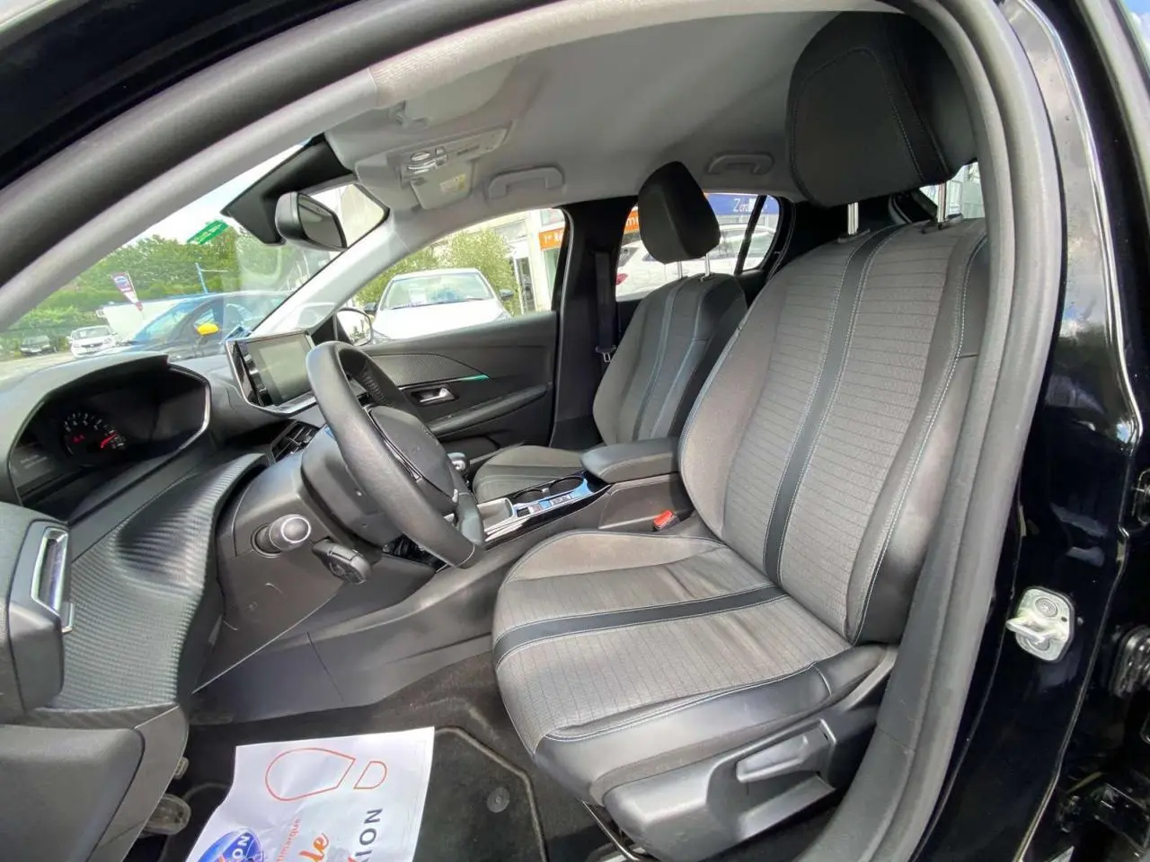 Vue intérieure côté conducteur de la Peugeot 208 noire 2021 avec sièges gris clair et tableau de bord moderne.