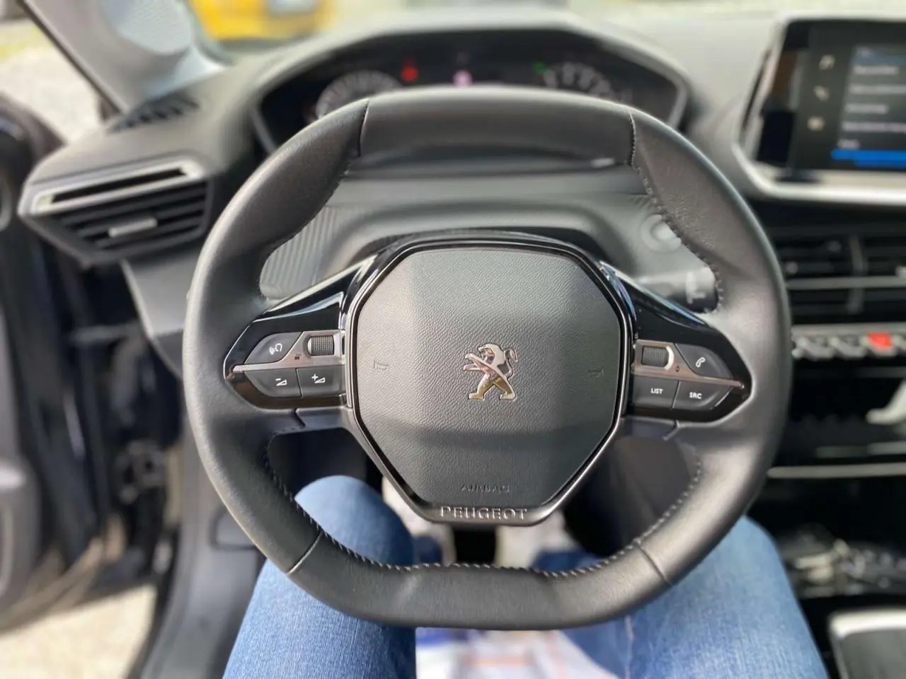 Vue centrée sur le volant cuir noir de la Peugeot 208 2021 avec commandes intégrées et tableau de bord en arrière-plan.
