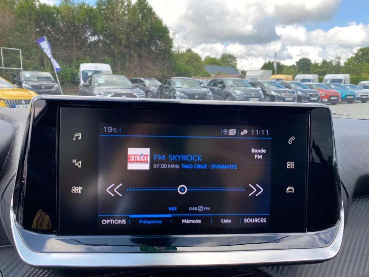 Écran tactile 7 pouces du tableau de bord de la Peugeot 208 noire, affichant la radio FM Skyrock en extérieur.