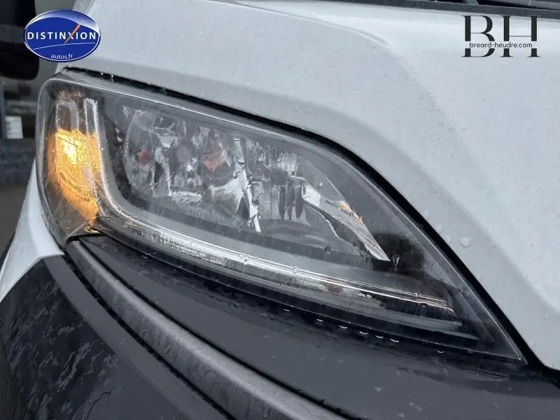 Gros plan sur le phare avant gauche du FIAT Ducato Benne blanc 2023 avec clignotant allumé et benne acier visible.