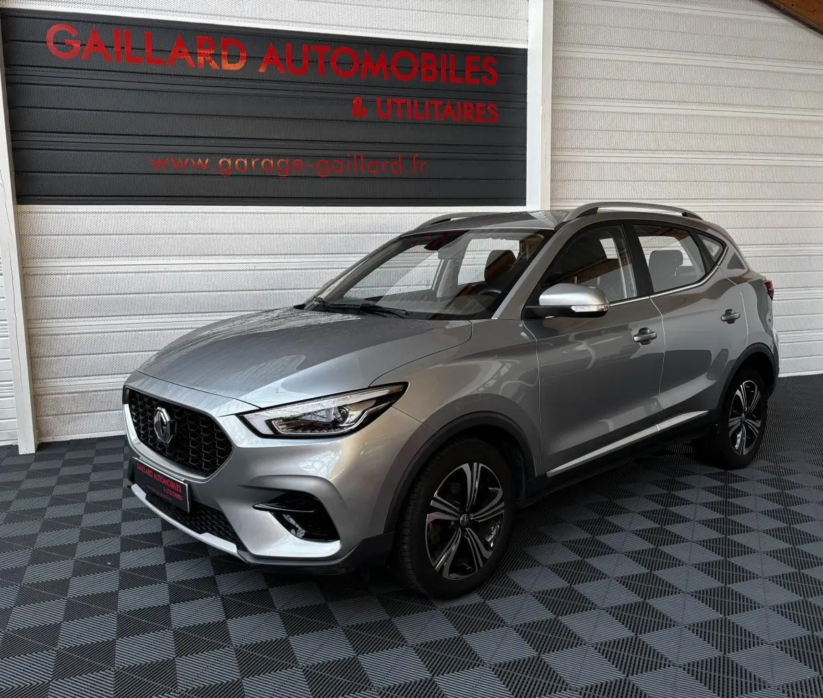 MG ZS gris clair vu en 3/4 avant droit dans un showroom avec jantes noires et toit ouvrant.